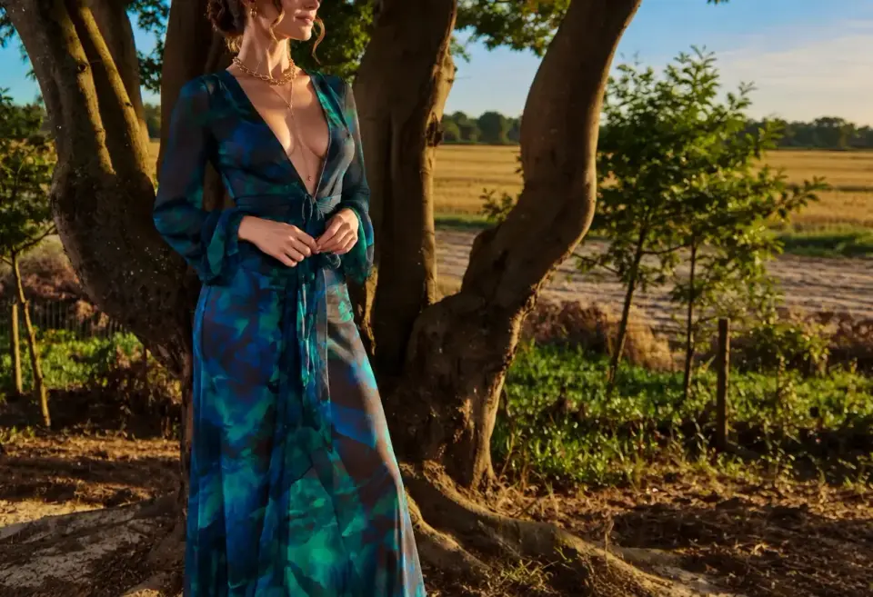 High-class escorts Sintra Portugal: elegant escort in a blue-green print gown beside a tree at sunset